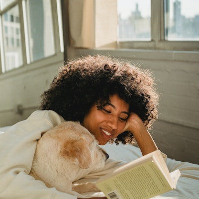 women reading a book on the bed with her dog